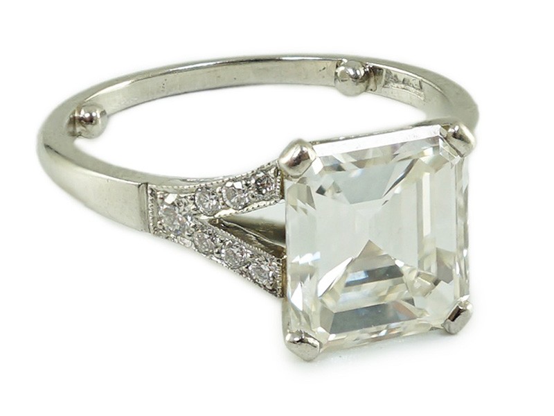 A platinum and single stone emerald cut diamond ring, with brilliant cut diamond set split shoulders